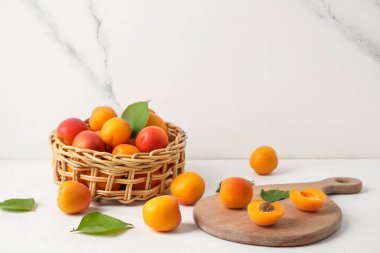 Tahta ve hasır kasede beyaz masada taze kayısılar var.