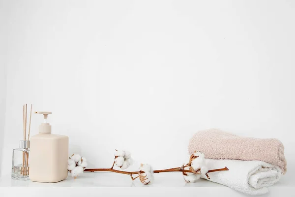 Cotton sprig with scented sticks, soap dispenser and towels on white shelf