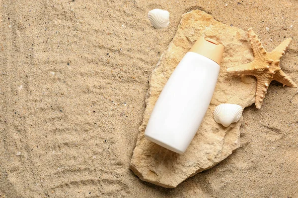 Bottle of sunscreen cream at stone with seashells and starfish on sand