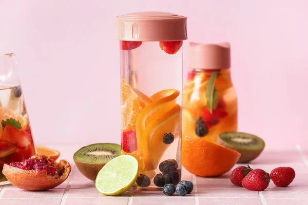 Sportflesjes Water Met Verschillende Gesneden Vruchten Roze Tegeltafel — Stockfoto