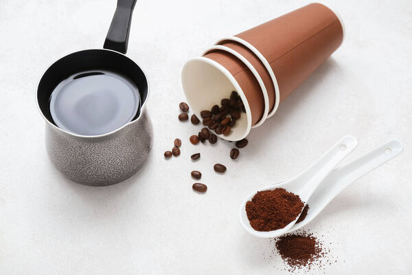 Cezve of hot espresso, spoons and cups with coffee beans on light background