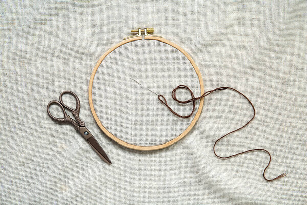 Wooden embroidery hoop with scissors, needle and canvas as background