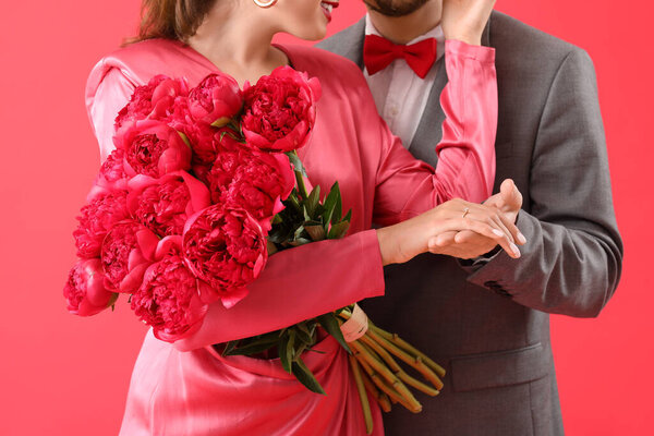Happy engaged couple with flowers on red background, closeup