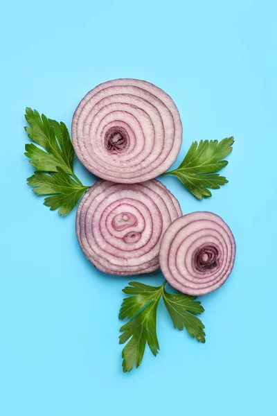 Fresh onion slices and parsley leaves on blue background