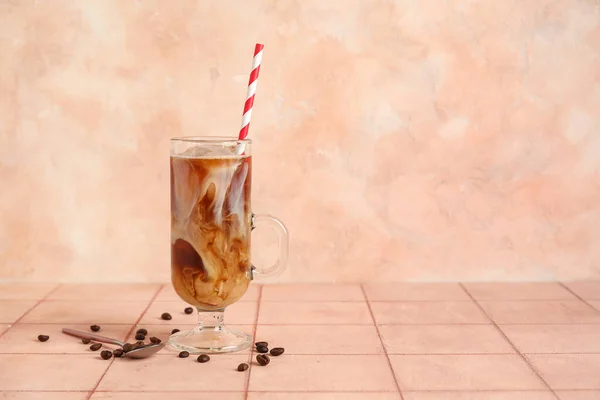壁の近くのベージュのタイルテーブルの上に藁 スプーン 豆と氷のコーヒーのガラス — ストック写真