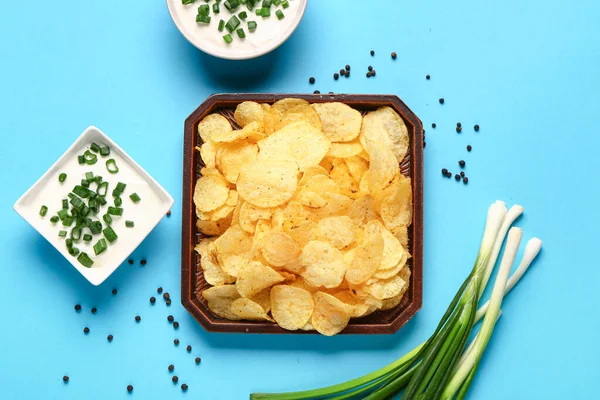 stock image Bowls of tasty sour cream with sliced green onion and potato chips on blue background