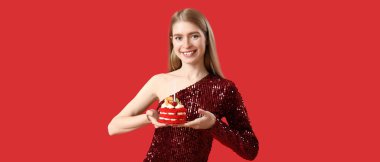 Kırmızı arka planda lezzetli doğum günü pastası olan güzel genç bir kadın. 