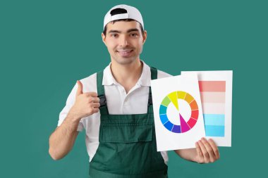 Renk paletleri olan erkek ressam yeşil arkaplanda başparmağını kaldırıyor
