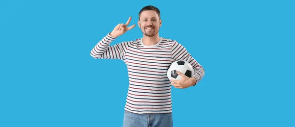 Człowiek Piłką Nożną Pokazując Gest Zwycięstwa Niebieskim Tle — Zdjęcie stockowe