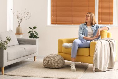 Young woman sitting in yellow armchair at home