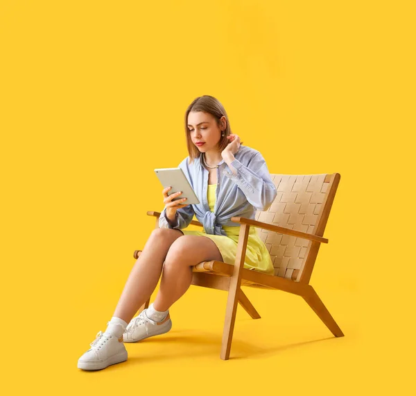 黄色の背景に木製のアームチェアでタブレットコンピュータを使用して若い女性 — ストック写真