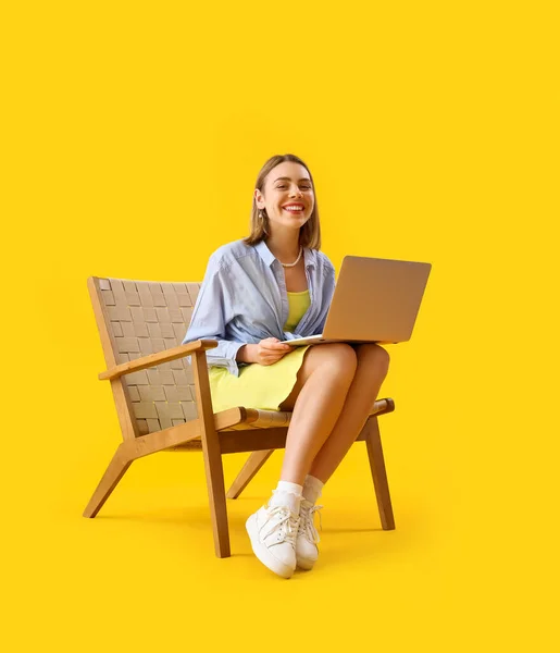 Junge Frau Mit Laptop Sitzt Holzsessel Auf Gelbem Hintergrund — Stockfoto