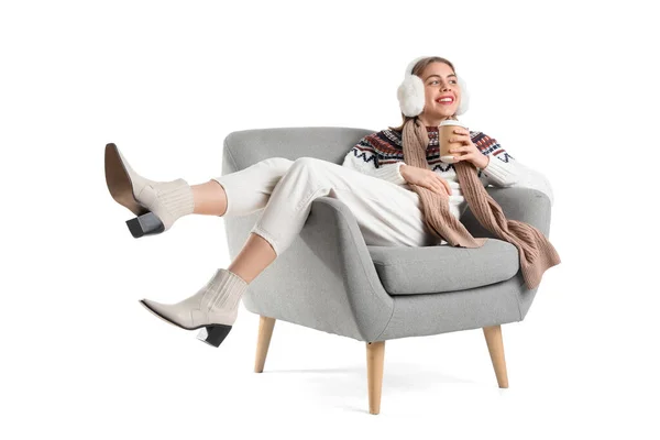 stock image Young woman with earmuffs and cup of coffee lying in grey armchair on white background