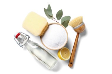 Beyaz arka planda bir kase kabartma tozu, sirke, temizlik fırçası, sünger ve limon.