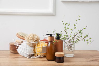 Işık duvarının yanındaki masada ağaç dalları olan banyo aksesuarları ve vazo.
