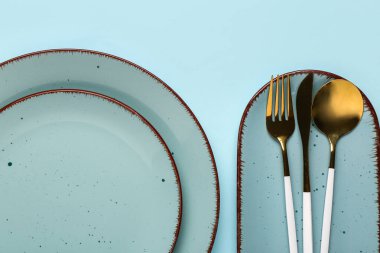 Mavi zemin üzerinde temiz tabaklar ve çatal bıçak takımı olan masa ayarları