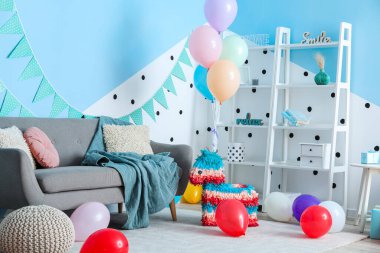 Doğum günü için dekore edilmiş oturma odasının içinde balonlar, pinyatalar ve çelenkler var.