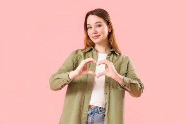 Güzel genç bir kadın ellerini pembe arka planda tutuyor.