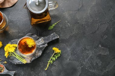 Bir bardak sağlıklı karahindiba çayı ve siyah arka planda çaydanlık.