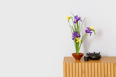 Aydınlık duvarın yanındaki masada çaydanlık ve fincanla çok güzel bir ikebana.