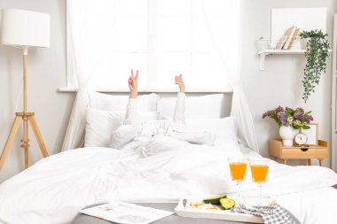 Genç bir kadının zafer jesti yaptığı ve yatakta baş parmağını kaldırdığı bir sabah.