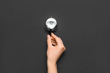 Büyüteçle kadın eli ve siyah arka planda parmak izi olan kağıt. Dedektif konsepti