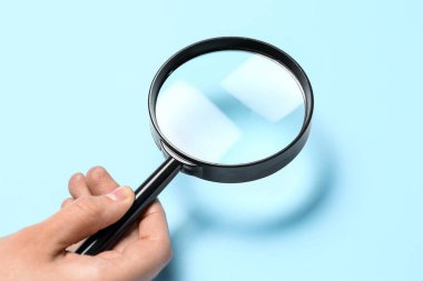 Mavi arka planda büyüteçle kadın eli