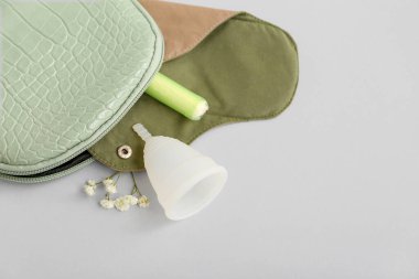 Tekrar kullanılabilir regl pedi, fincanı ve gri arka planda tamponu olan kadının makyaj çantası.