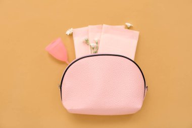 Kadının makyaj çantası, regl fincanı ve kahverengi arka plan pedleri.