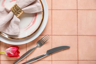 Katlanmış peçete, çatal bıçak takımı ve pembe fayanslı lale çiçekli tabaklar.
