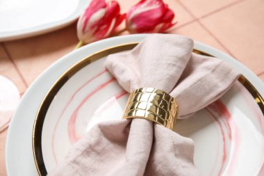 Katlanmış peçete, çatal bıçak takımı ve pembe fayanslı lale çiçekli tabaklar.