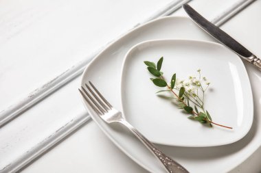 Gümüş çatal bıçaklı tabaklar ve beyaz ahşap arka planda çiçekler.