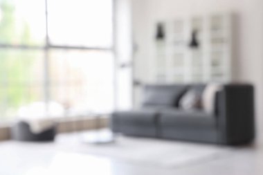 Büyük pencerenin yanında rahat gri kanepe ve kahve masası olan aydınlık oturma odasının içi bulanık manzaralı.