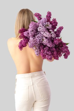 Açık arkaplanda leylak çiçekleri olan genç bir kadın.