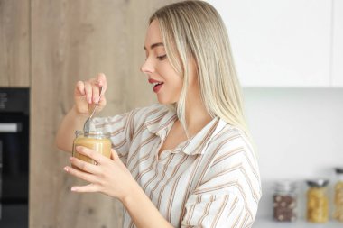 Mutfakta kaşığı ve fındık ezmesi dolu bir kavanozu olan genç kadın.