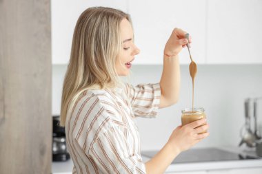 Mutfakta kaşığı ve fındık ezmesi dolu bir kavanozu olan genç kadın.