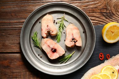 Ahşap zemin üzerinde çiğ morina balığı parçaları olan bir tabak.