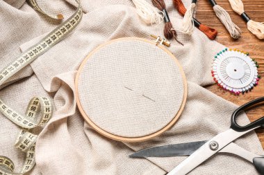 Kahverengi ahşap arka planda işlemeli çember, küflü iplikler ve makas.