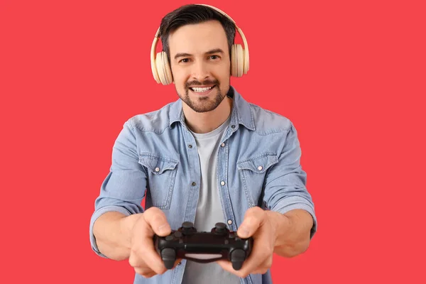 Schöner Mann Mit Kopfhörer Und Spielkissen Auf Rotem Hintergrund — Stockfoto