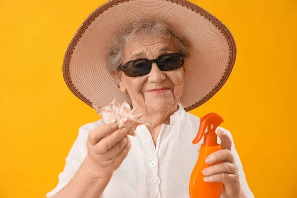 日焼け止めクリームとオレンジの背景に貝殻を持つシニア女性 クローズアップ — ストック写真