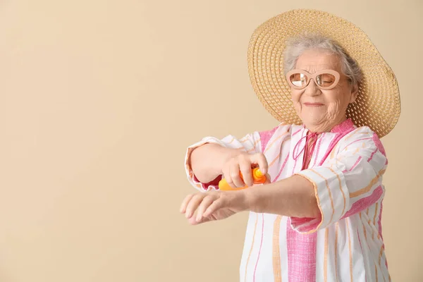 Seniorin Trägt Sonnencreme Auf Beigem Hintergrund Auf — Stockfoto