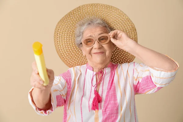 ベージュの背景に日焼け止めクリームを持つシニア女性 — ストック写真