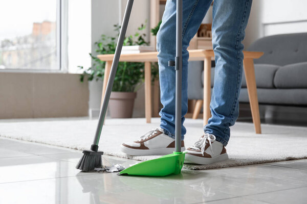 Young man sweeping floor with broom at home