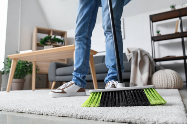 Young man sweeping carpet with broom at home, closeup