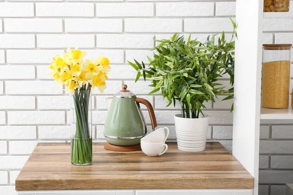 開花ナルシシズムの花と花瓶 電気ケトル キッチンカウンターのカップと観葉植物 — ストック写真