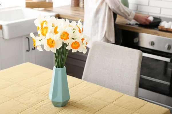 Woman cooking in modern kitchen with narcissus flowers on table