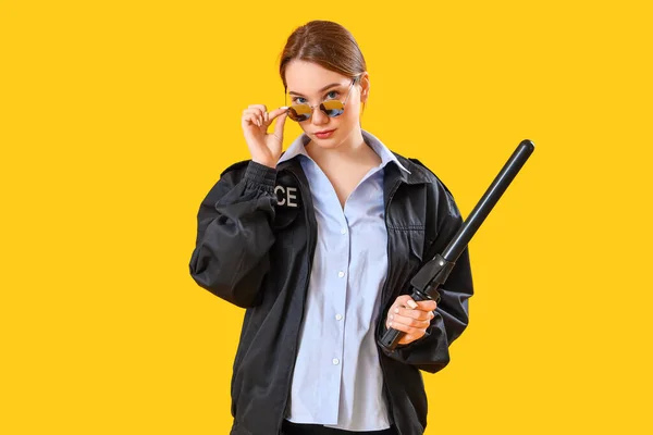 黄色の背景にバトンを持つ女性警察官 — ストック写真