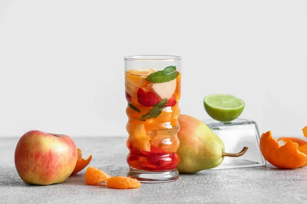 在灰色桌子上倒入不同切片水果的一杯水 — 图库照片