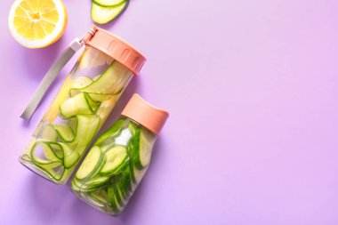 Salatalık dilimleri ve leylak arkaplanlı spor şişeleri.