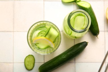 Beyaz fayans masasında salatalık dilimleri ile doldurulmuş bardak ve bir şişe su.